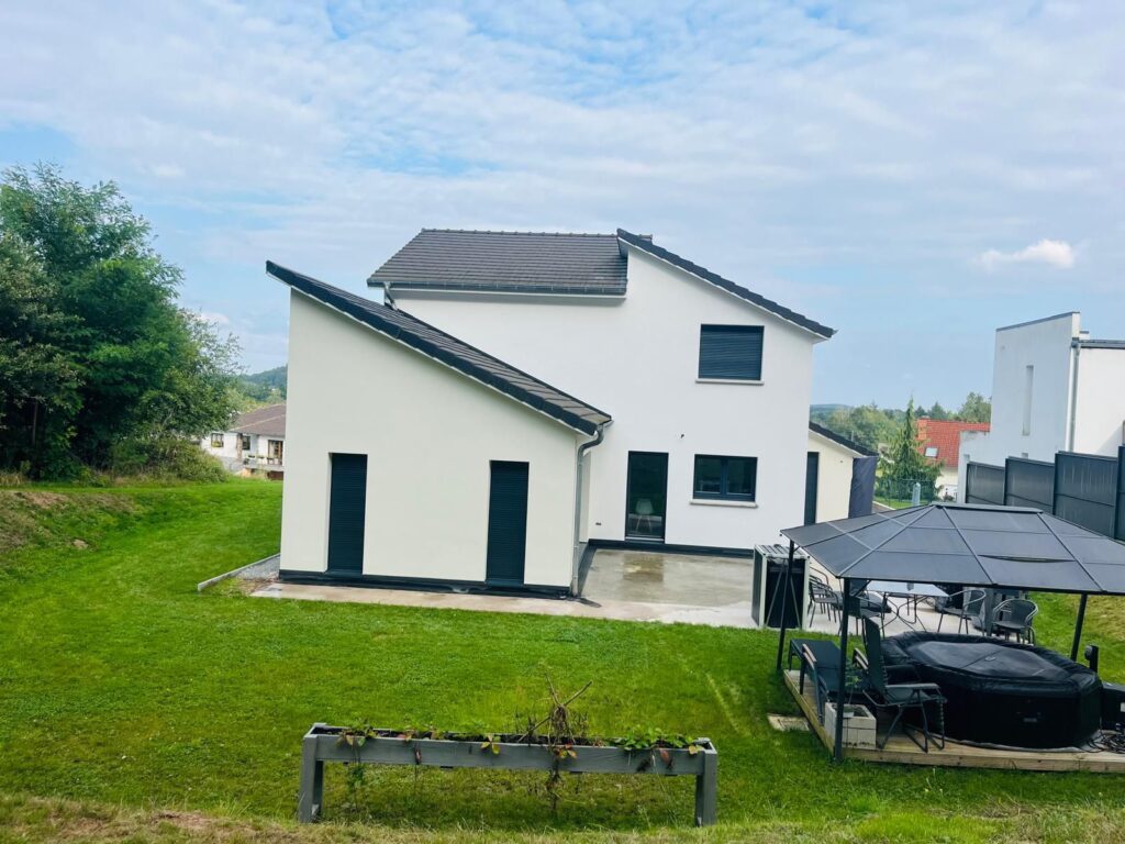 Maison moderne blanche et noire avec toiture gris anthracite, terrasse et piscine, entourée d'un jardin verdoyant