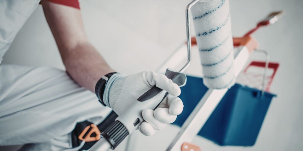 Peintre professionnel tenant un pinceau avec gants de protection blancs et striés bleus, outil de peinture en main